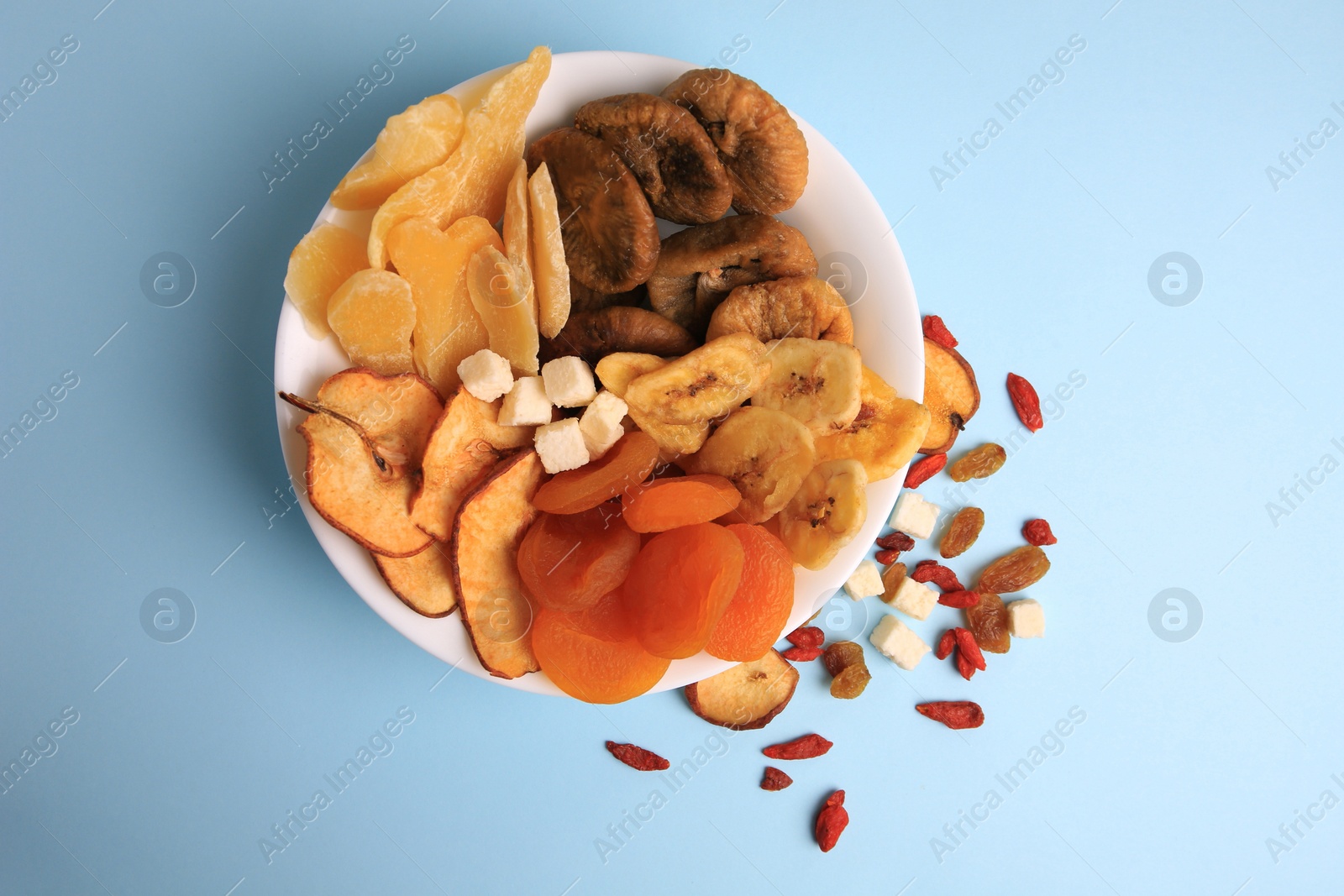 Photo of Bowl with different dried fruits on light blue background, flat lay