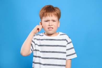 Photo of Little boy suffering from ear pain on light blue background