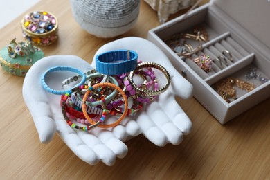 Photo of Ceramic hand stand with many stylish bracelets and jewelry boxes on wooden table