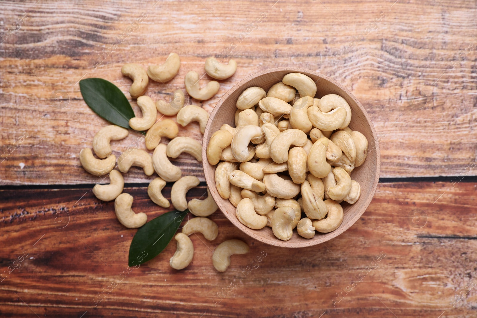 Photo of Tasty cashew nuts and green leaves on wooden table, top view