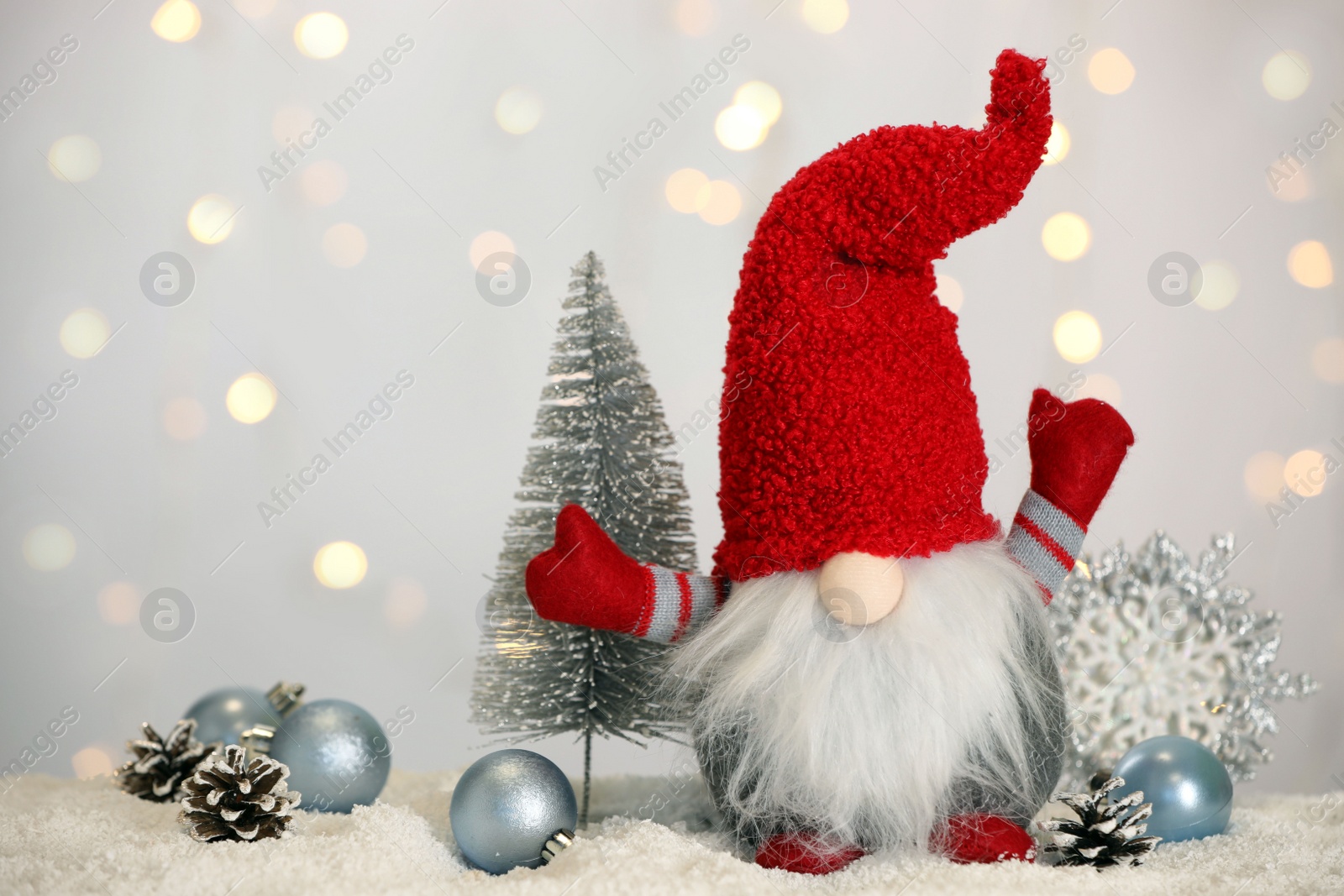 Photo of Cute Christmas gnome and festive decor on snow against blurred lights