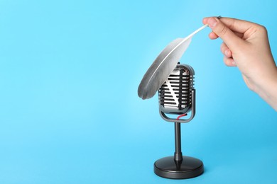 Photo of Woman making ASMR sounds with microphone and feather on light blue background, closeup. Space for text