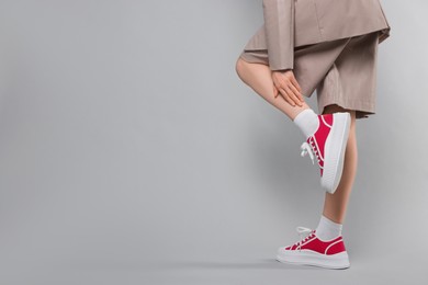 Woman posing in red classic old school sneakers on light gray background, closeup. Space for text