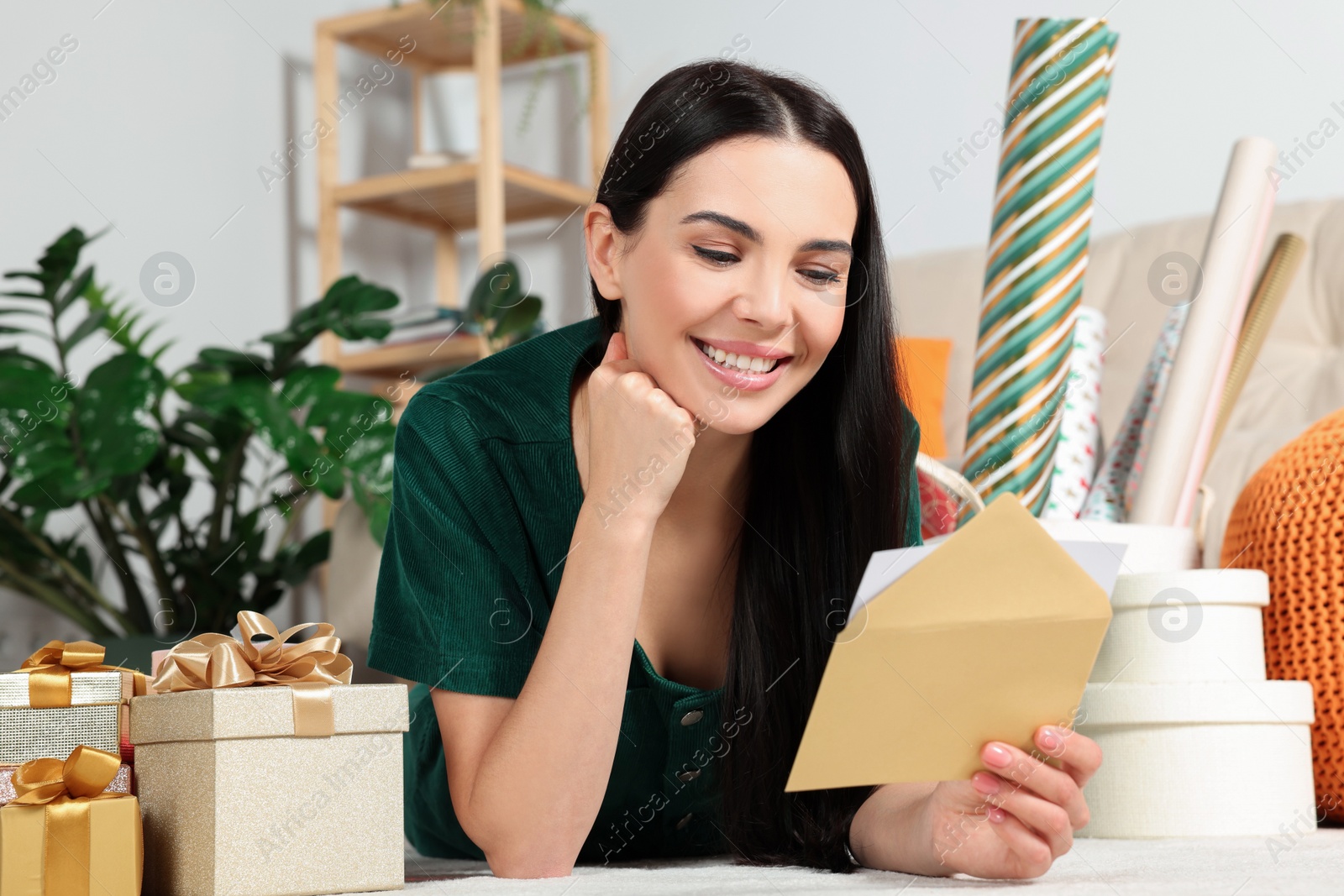 Photo of Happy woman reading greeting card on floor in living room