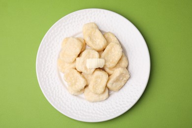 Plate of tasty lazy dumplings with butter on light green background, top view