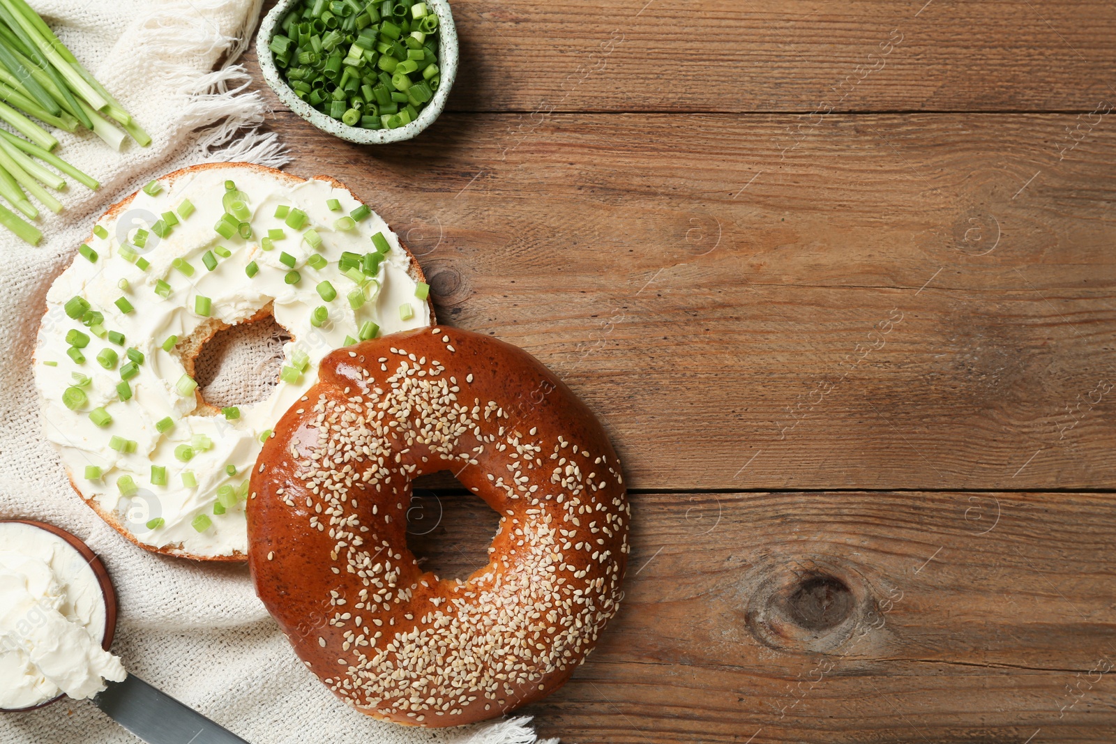Photo of Delicious bagel with cream cheese and green onion on wooden table, flat lay. Space for text