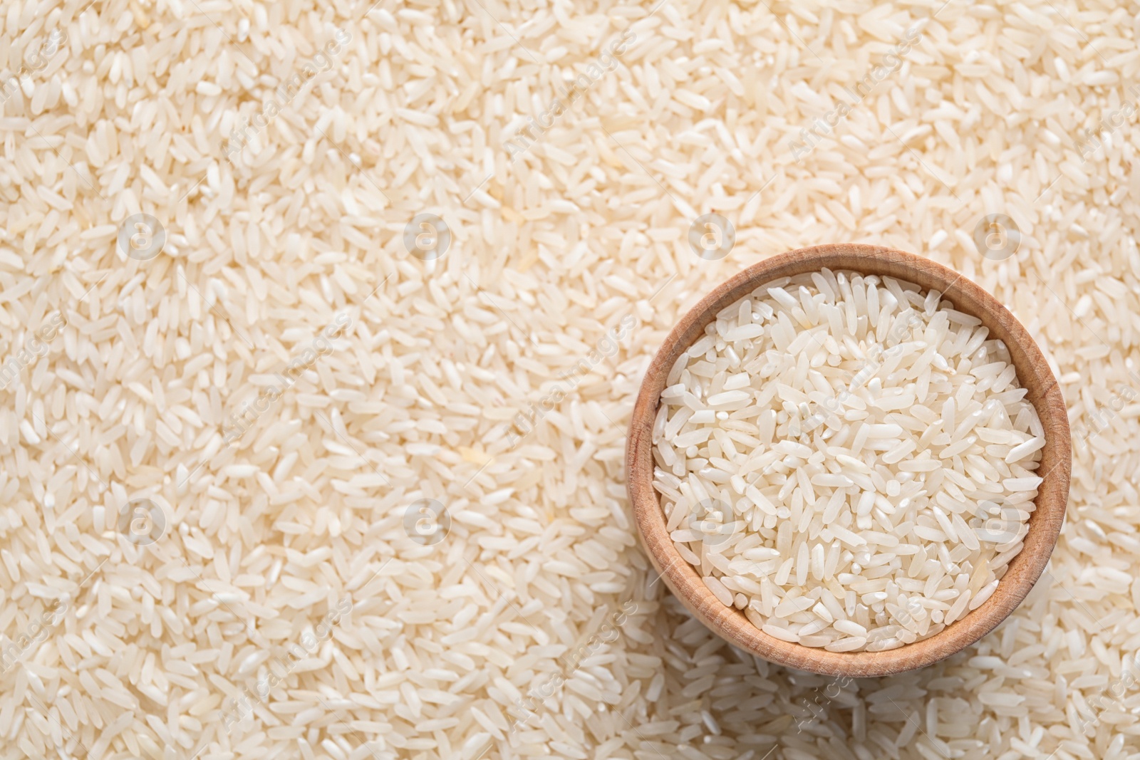 Photo of Pile of polished rice and wooden bowl, top view. Space for text