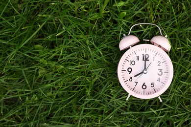 Photo of Pink small alarm clock on green grass outdoors, top view. Space for text