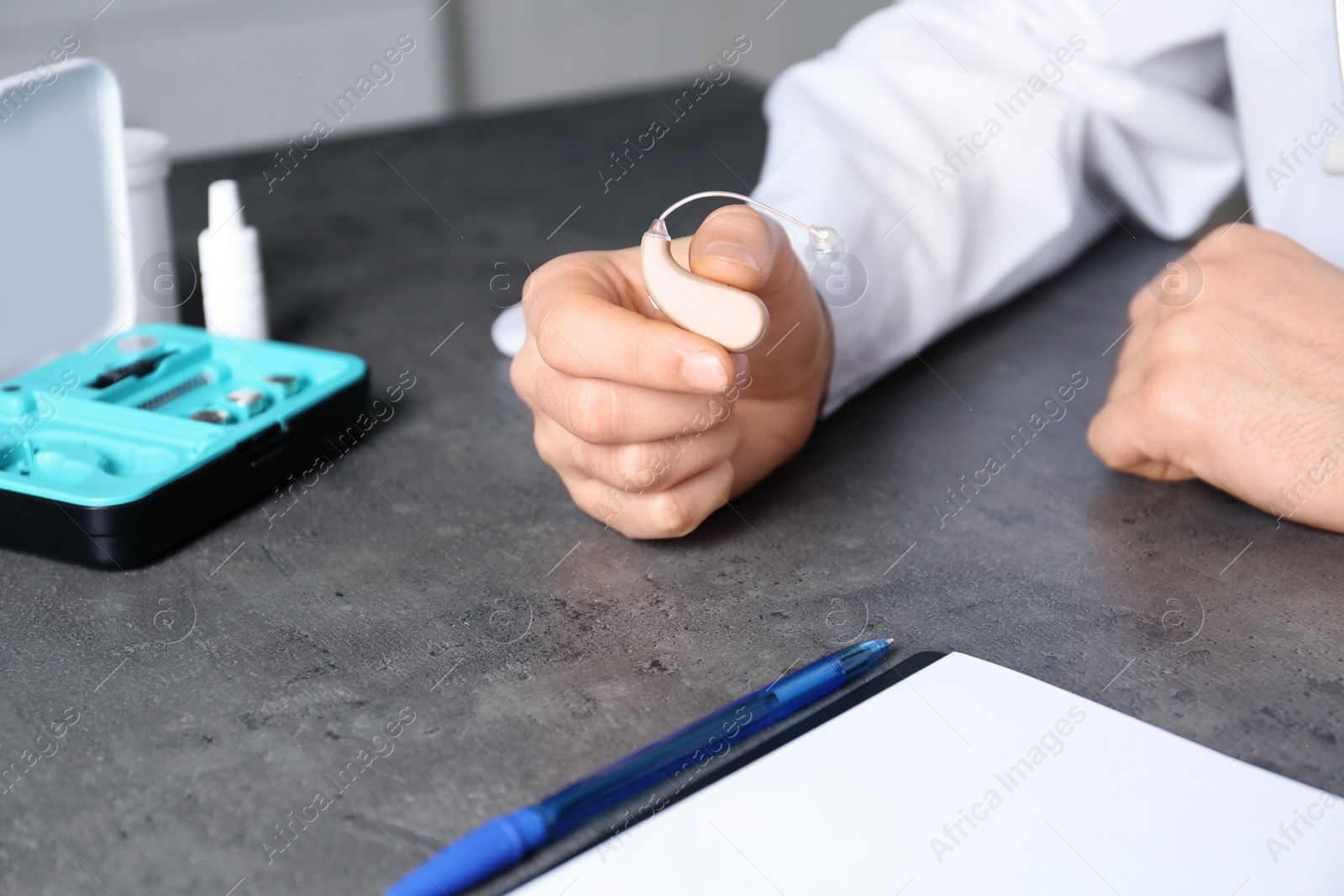 Photo of Doctor holding hearing aid at table, closeup. Medical objects