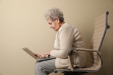 Photo of Elderly woman with poor posture using laptop on beige background