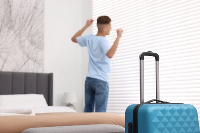 Photo of Guest stretching in stylish hotel room, focus on suitcase