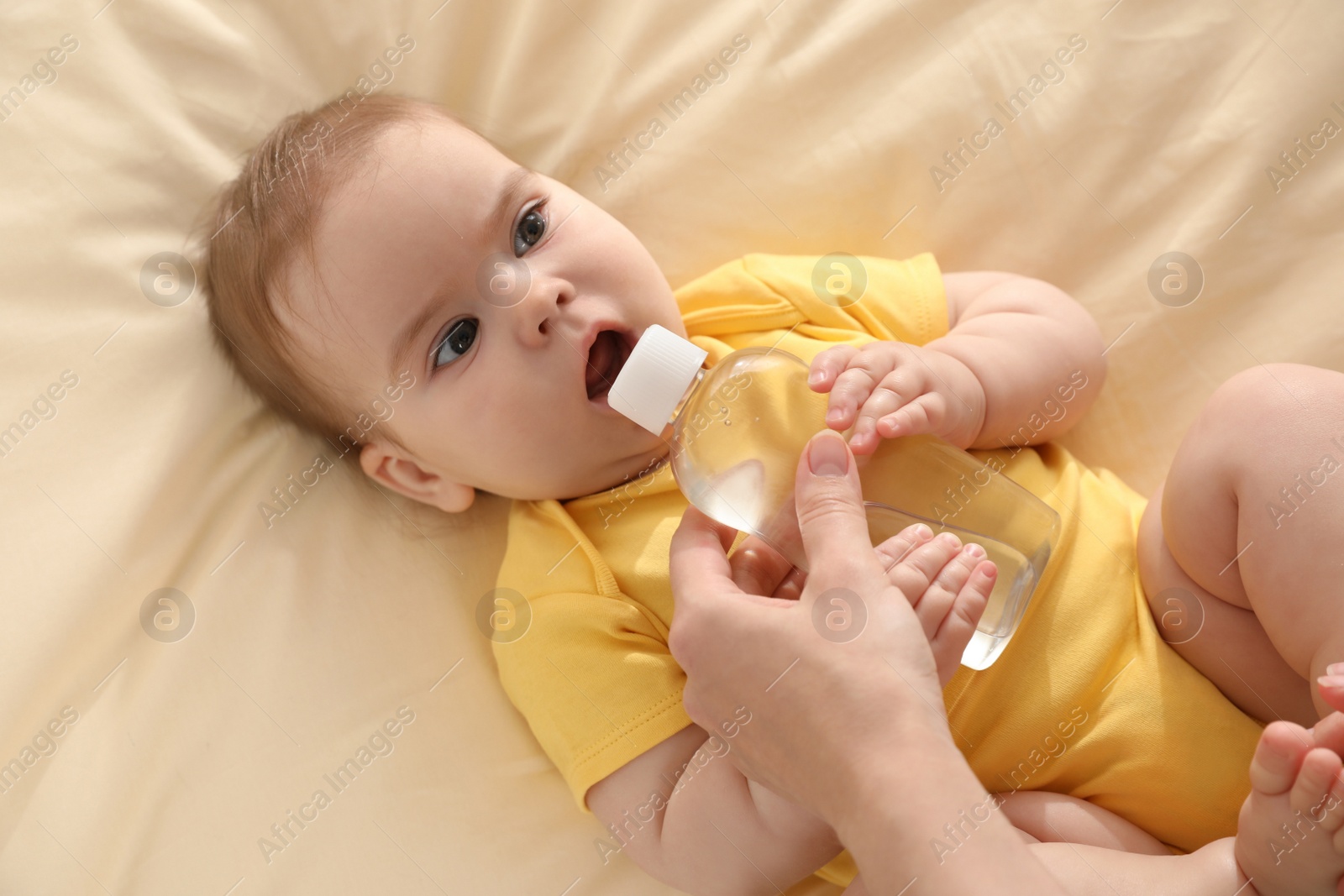 Photo of Mother and baby with bottle of massage oil on bed, top view