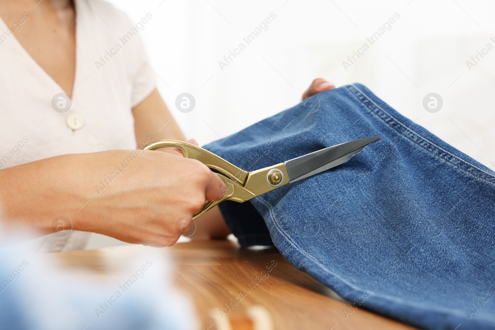 Photo of Woman cutting jeans with scissors at wooden table indoors, closeup