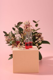 Photo of Stylish presentation of skincare ampoules and flowers on pink background