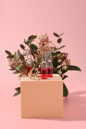 Stylish presentation of skincare ampoules and flowers on pink background