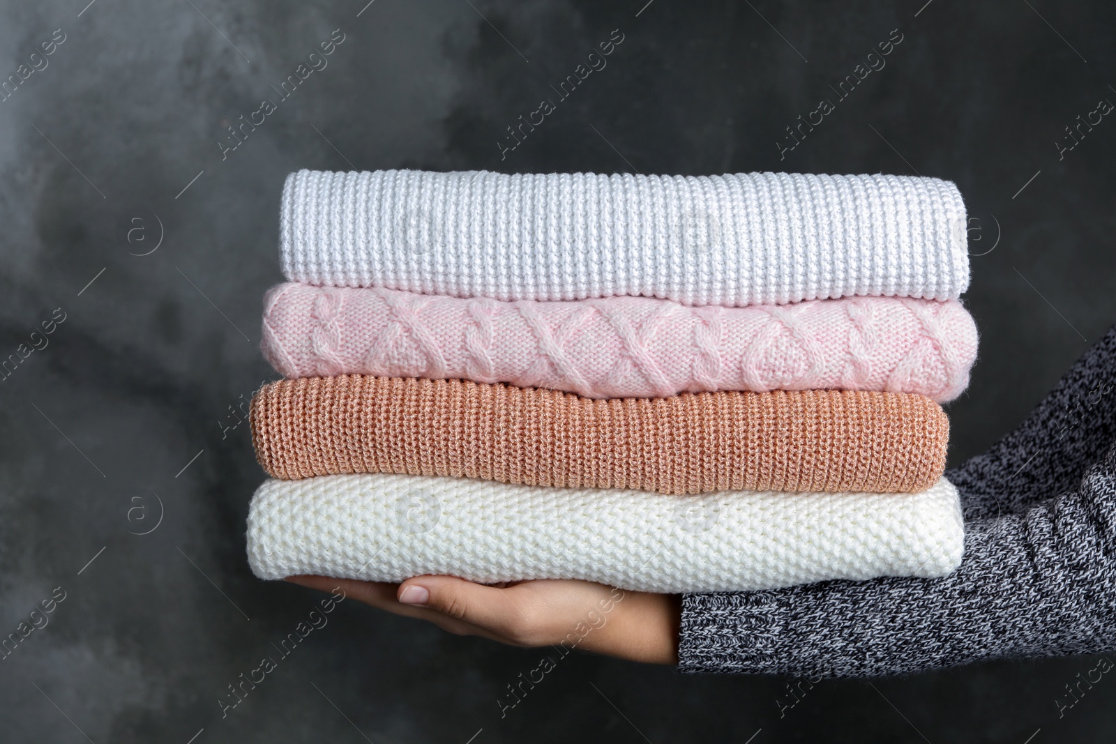 Photo of Woman holding stack of warm clothes on dark background, closeup. Autumn season