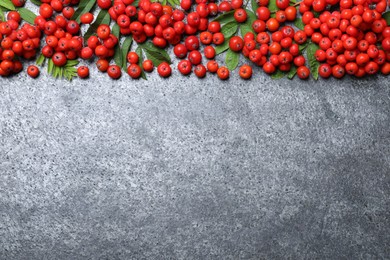 Photo of Fresh ripe rowan berries and green leaves on grey table, flat lay. Space for text