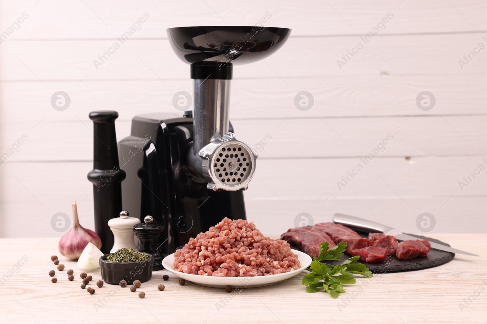 Photo of Electric meat grinder with beef, spices and parsley on white wooden table