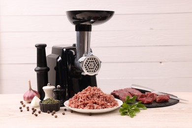 Electric meat grinder with beef, spices and parsley on white wooden table