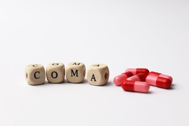 Wooden cubes with word Coma and pills on grey background, closeup