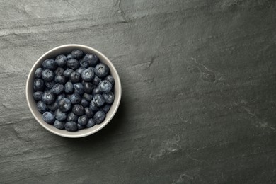 Photo of Ceramic bowl with blueberries on black table, top view and space for text. Cooking utensil