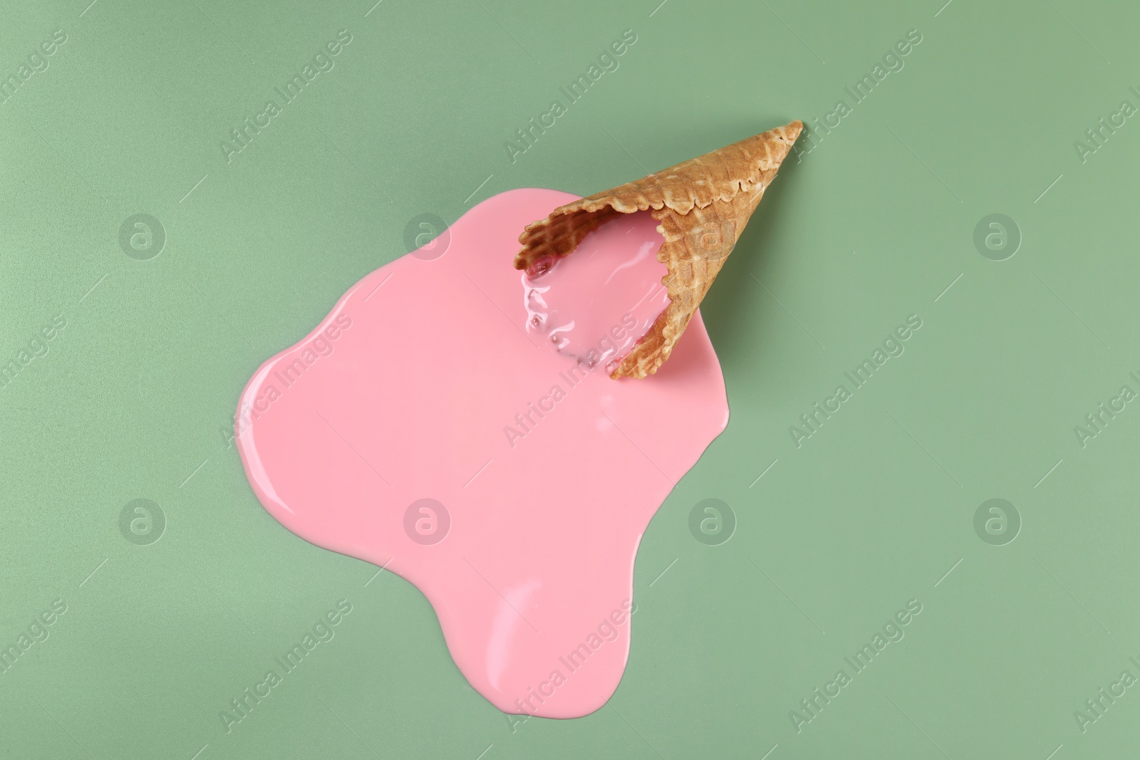 Photo of Melted ice cream and wafer cone on green background, top view