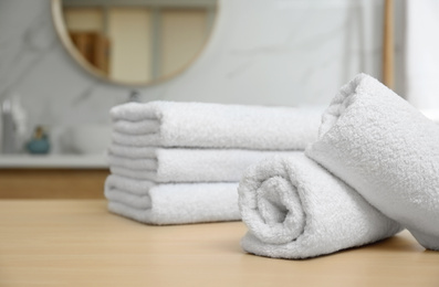 Photo of White fresh towels on wooden table in bathroom, closeup