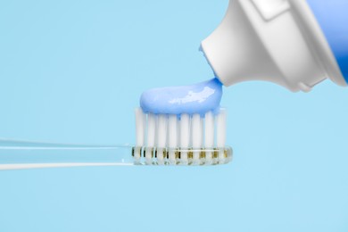Photo of Squeezing toothpaste onto electric toothbrush on light blue background, closeup
