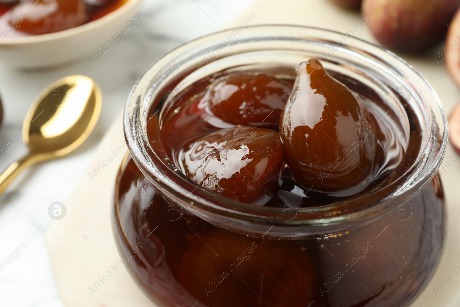Photo of Jar of tasty sweet fig jam on white marble table, closeup