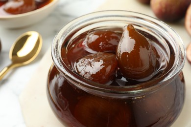 Photo of Jar of tasty sweet fig jam on white marble table, closeup