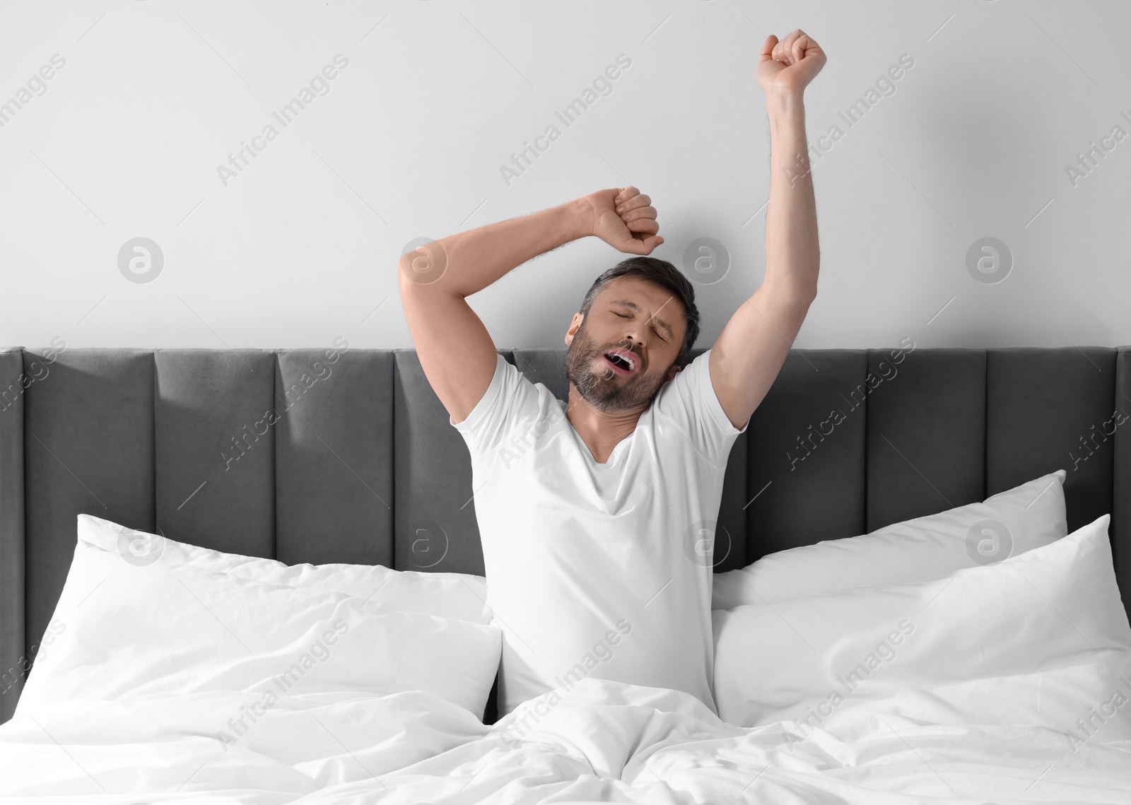 Photo of Sleepy man stretching in soft bed at home in morning