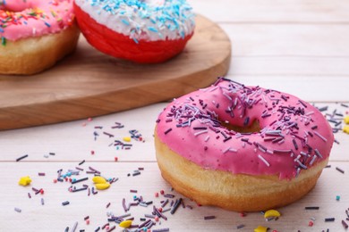 Glazed donuts decorated with sprinkles on white wooden table, closeup. Space for text. Tasty confectionery