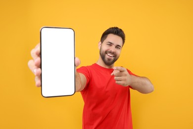 Photo of Young man showing smartphone in hand and pointing at it on yellow background