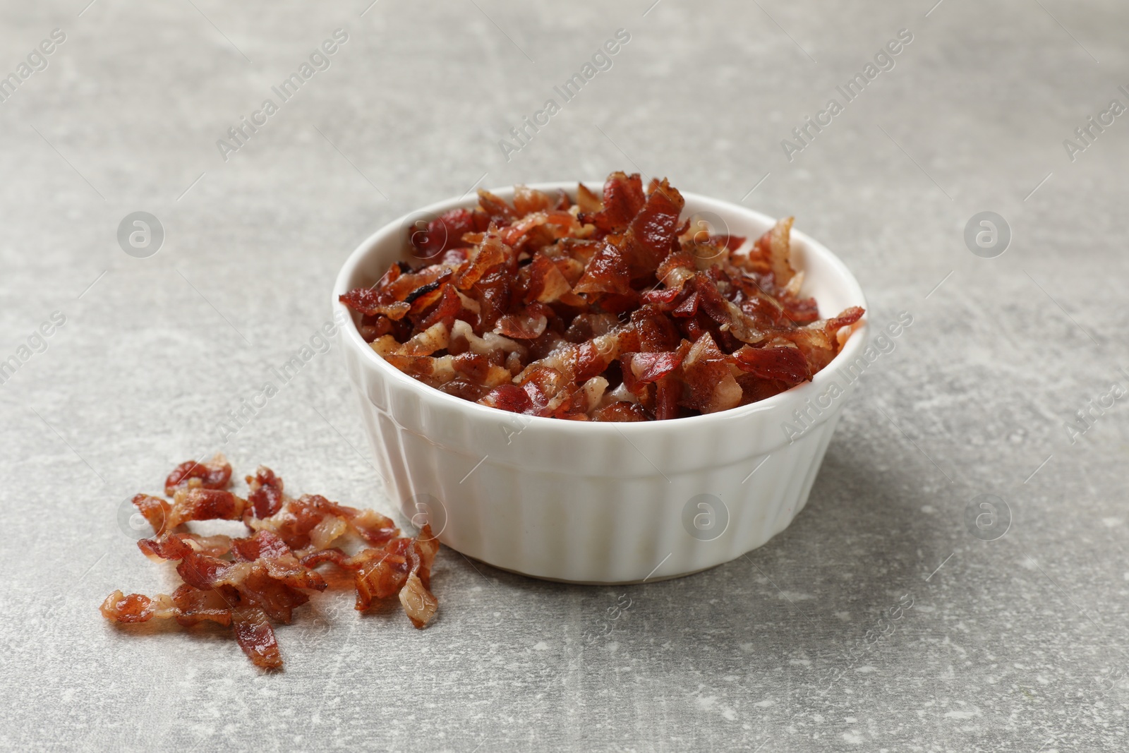 Photo of Pieces of tasty fried bacon in bowl on gray textured table