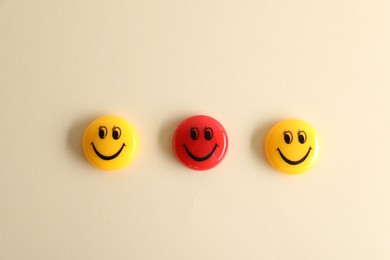 Photo of Choice concept. Red and yellow magnets with happy emoticons on beige background, flat lay