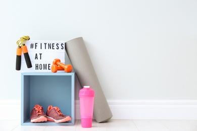 Photo of Sport equipment and lightbox with hashtag FITNESS AT HOME on floor indoors, space for text. Message to promote self-isolation during COVID‑19 pandemic
