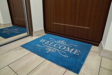 Photo of Beautiful blue doormat with word Welcome on floor near entrance