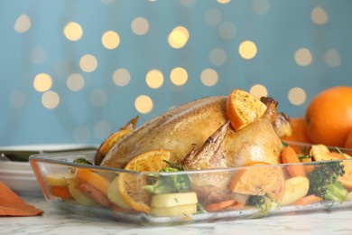 Delicious chicken with oranges and vegetables on white marble table against blurred festive lights