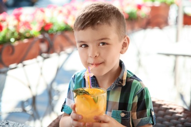 Cute boy with glass of natural lemonade in cafe