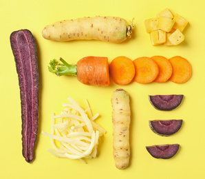 Photo of Whole and cut raw color carrots on yellow background, flat lay