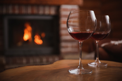 Glasses of red wine near fireplace indoors. Space for text