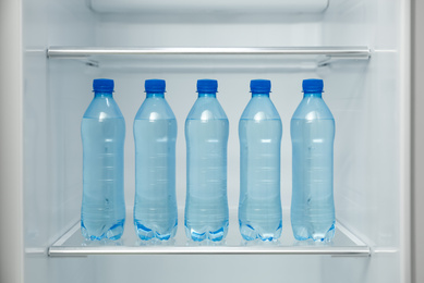 Photo of Many bottles with fresh water on fridge shelf