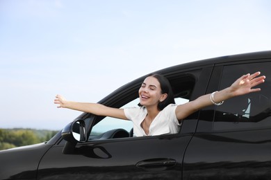 Photo of Enjoying trip. Happy woman leaning out of car window outdoors