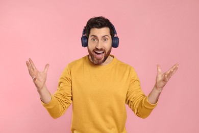 Emotional man listening music with headphones on pink background