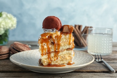 Photo of Piece of delicious homemade cake with caramel sauce and macaron on table