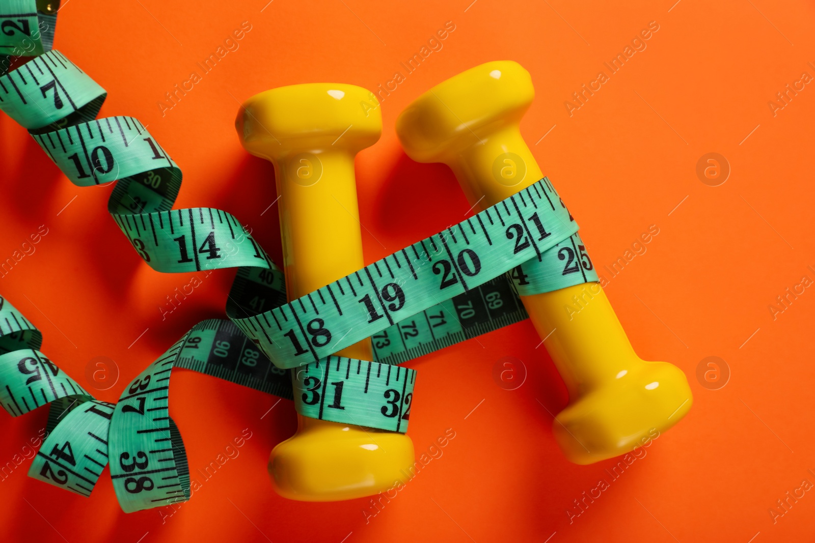 Photo of Dumbbells and measuring tape on orange background, flat lay. Weight loss concept