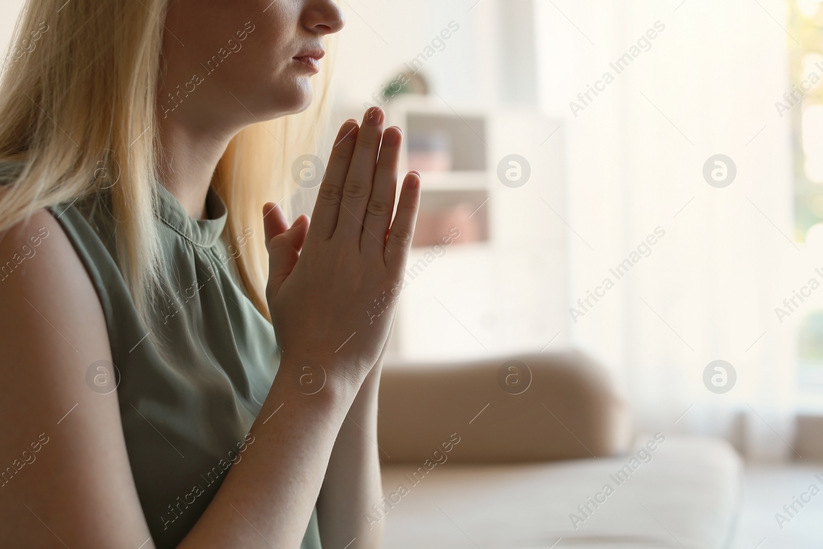 Photo of Religious young woman praying at home. Space for text