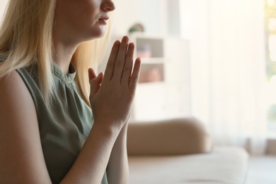 Photo of Religious young woman praying at home. Space for text