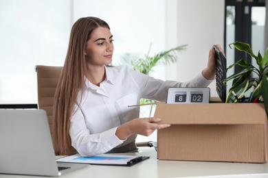 Photo of Happy young woman packing stuff in box at office