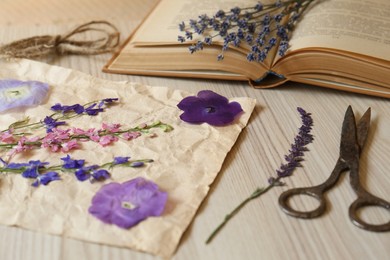 Photo of Beautiful dried flowers, book and scissors on wooden table, closeup